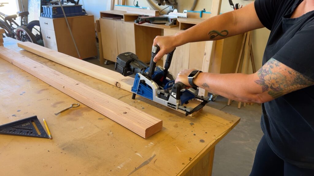 Woman using a pocket hole jig to drill holes in a wood board for a DIY 6 foot mobile workbench frame.