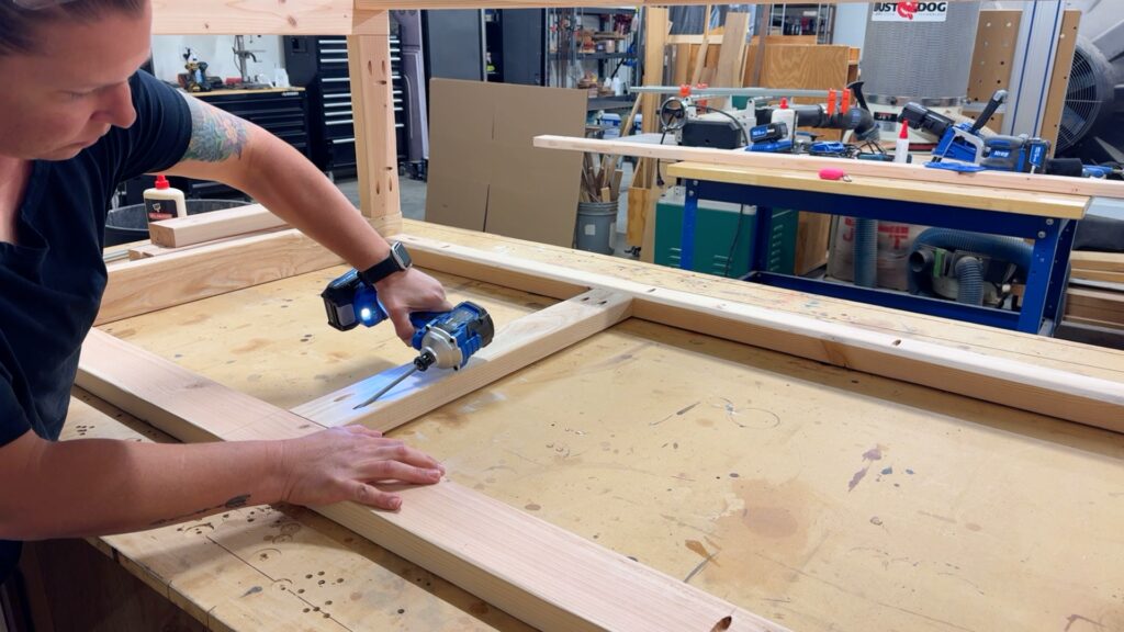 Attaching vertical support boards to the workbench frame with a drill during mobile workbench construction.