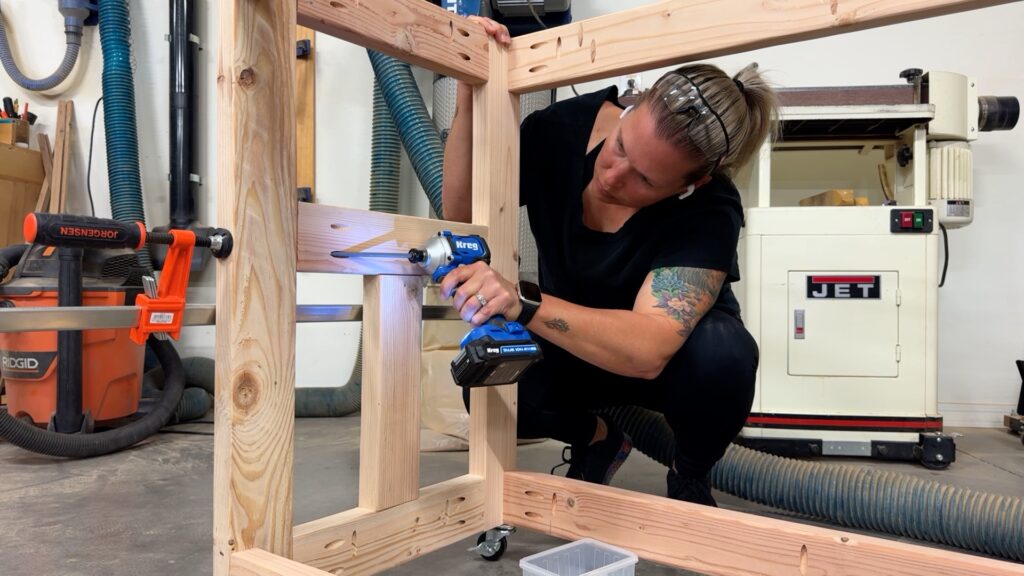 Securing lower shelf supports inside the workbench frame with a drill during assembly.