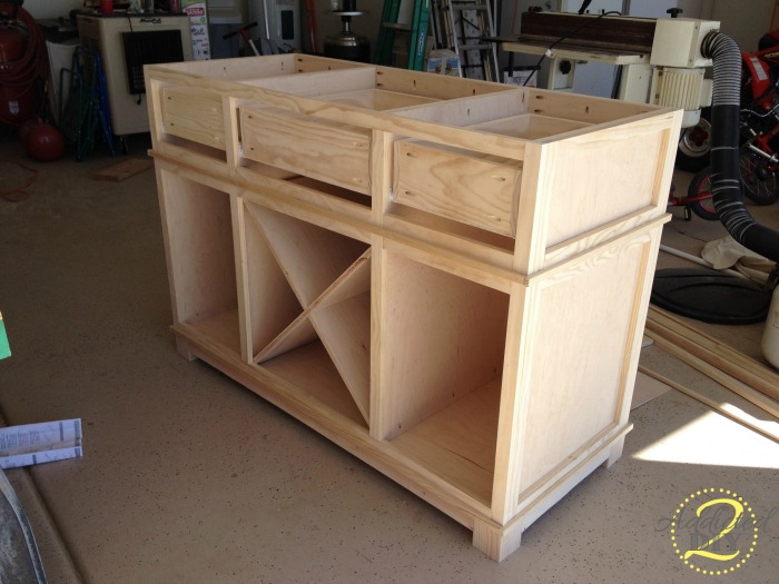 Unfinished DIY kitchen island with drawer boxes, face trim, and decorative X shelf installed