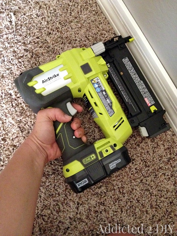 Using a cordless brad nailer to install baseboards along wall