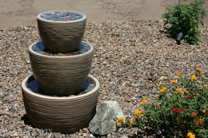 Three-tier outdoor water fountain made from pots surrounded by desert landscaping and flowering plants