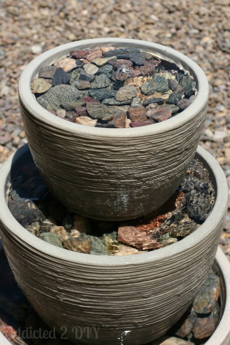Close-up of tiered water fountain showing water flowing over stacked pots filled with decorative rocks
