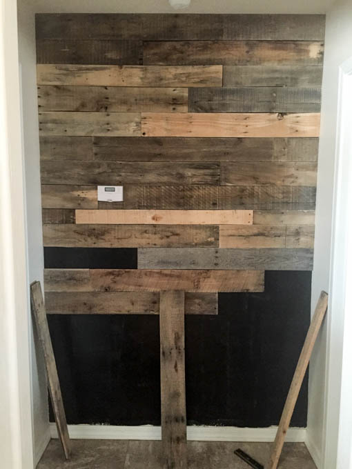 Midway through pallet wall installation showing staggered wood plank pattern