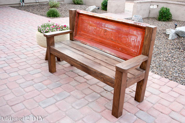 Angled view of a DIY rustic wood bench with a vintage red Chevrolet tailgate used as the bench back.