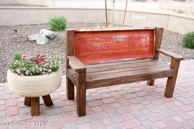 Front angled view of a finished tailgate bench beside a flower planter in a desert backyard landscape.