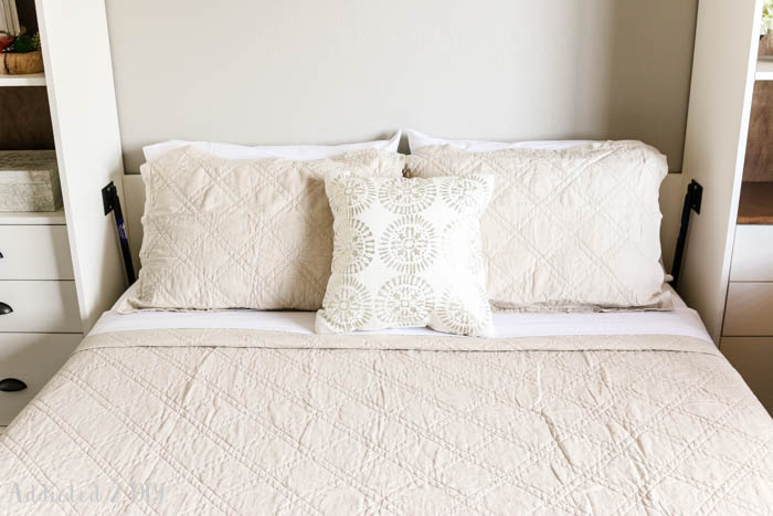 Close-up of Murphy bed bedding with neutral quilt and decorative pillows