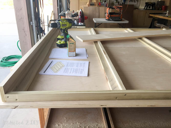 Murphy bed frame assembly with tools and instructions laid out on plywood