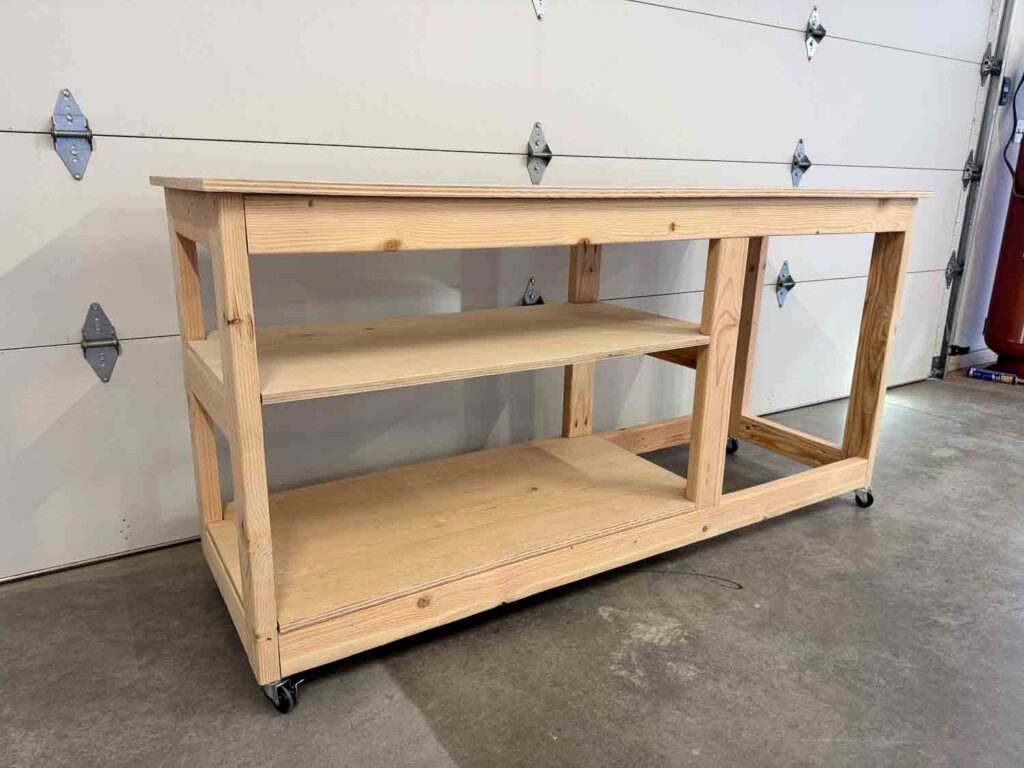 DIY rolling workbench with open shelving and wood frame on wheels in a garage workspace.