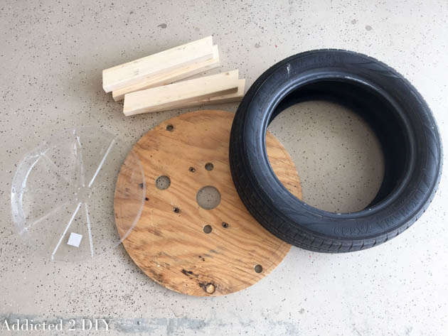 Materials for building a DIY tire planter including an old tire, wood base, legs, and plastic liner