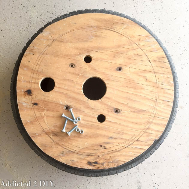 Wood base fitted inside an old tire with bolts and holes marked for assembly