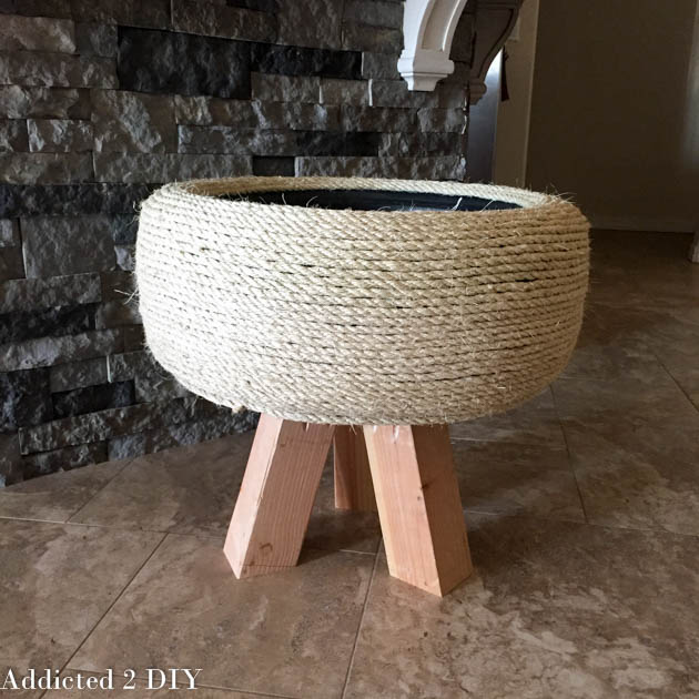 Unfinished DIY tire planter with rope wrapping and attached wooden legs indoors