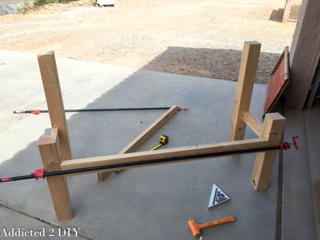 Bench frame in progress with 4x4 legs and side rails clamped together during assembly on a driveway.