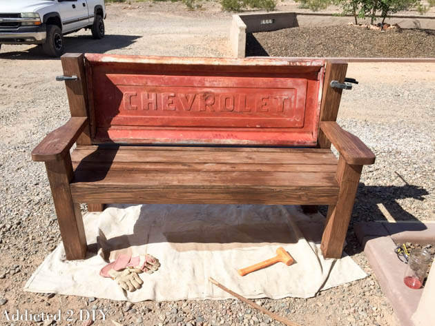 Tailgate bench outdoors during staining and finishing, showing the red Chevrolet tailgate and dark stained wood frame.