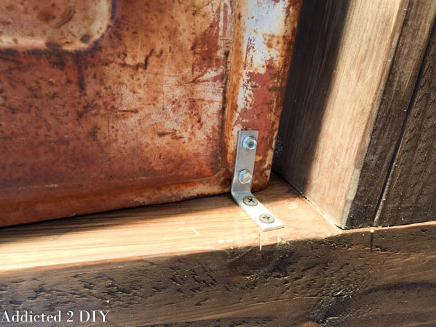 Close-up of a metal angle bracket securing the bottom corner of the tailgate to the wooden bench frame.