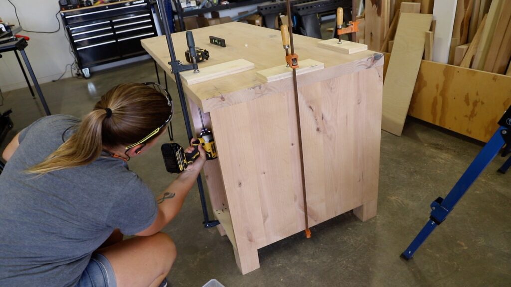 Attaching a wood cabinet base to a solid wood desktop using clamps and a drill