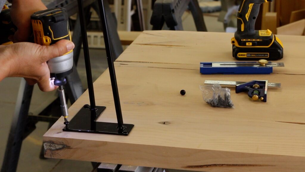 Screwing black hairpin legs to the underside of a solid wood desk with a cordless drill