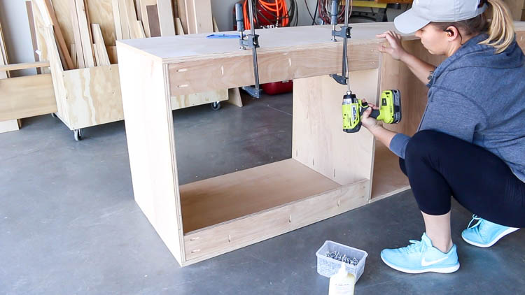 Attaching rear stabilizing stretchers to a DIY miter saw bench cabinet with a drill and clamps