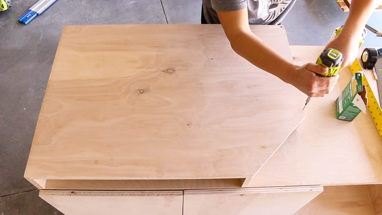 Attaching the plywood table top to a DIY miter saw bench frame with wood screws and a drill