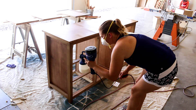 Spraying polycrylic topcoat on a DIY rustic dresser using a Finish Max paint sprayer in a workshop