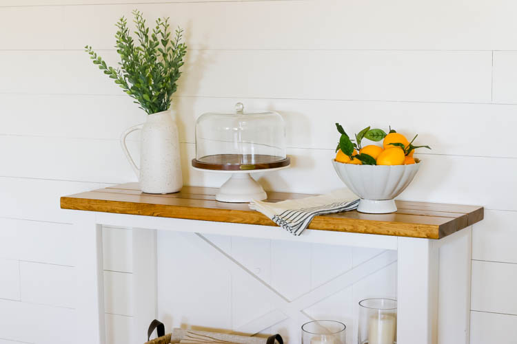 Close-up of stained wood top on white DIY farmhouse console table styled with home decor