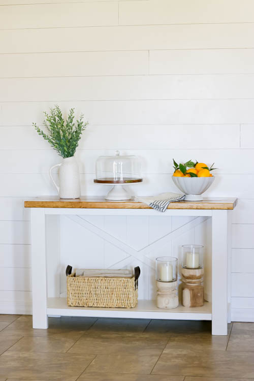 DIY farmhouse console table with bottom shelf styled with basket and candles against shiplap wall