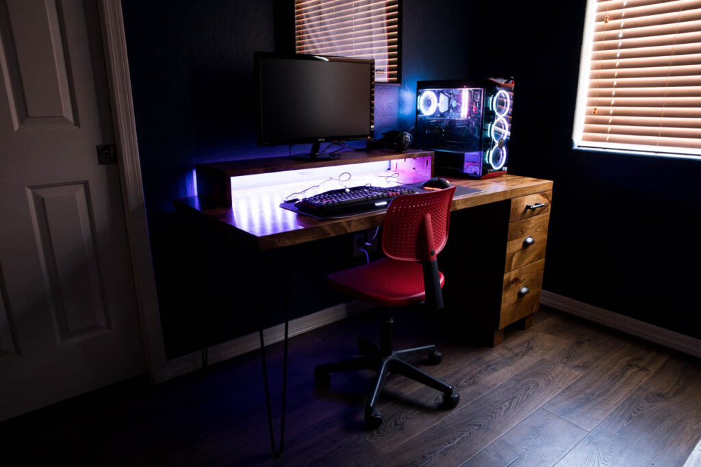 Finished DIY gaming desk with LED lighting glowing under the monitor shelf in a dark room