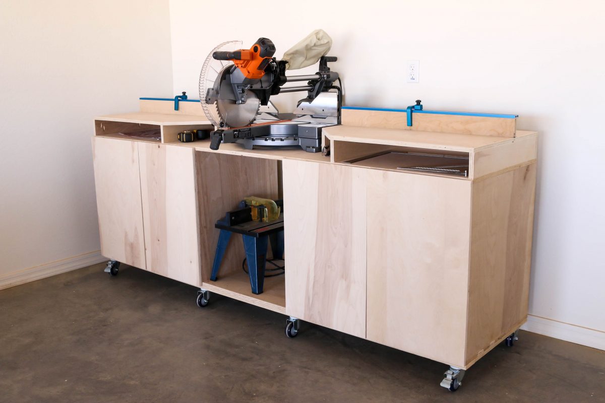 Completed DIY mobile miter saw bench with cabinet doors, locking casters, and T-track fence — three-quarter view