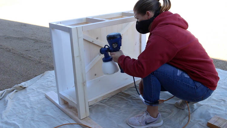 Spray painting farmhouse console table base white with paint sprayer outdoors