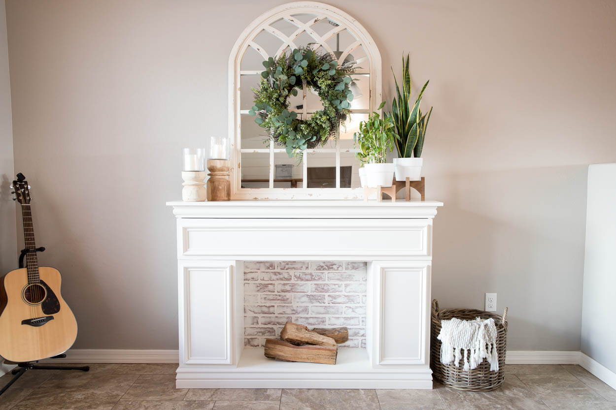 finished DIY faux fireplace with storage and faux brick backing styled with mirror, plants, and decor