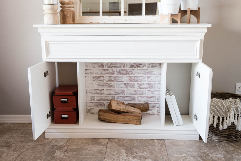 DIY faux fireplace with cabinet doors open showing interior storage compartments