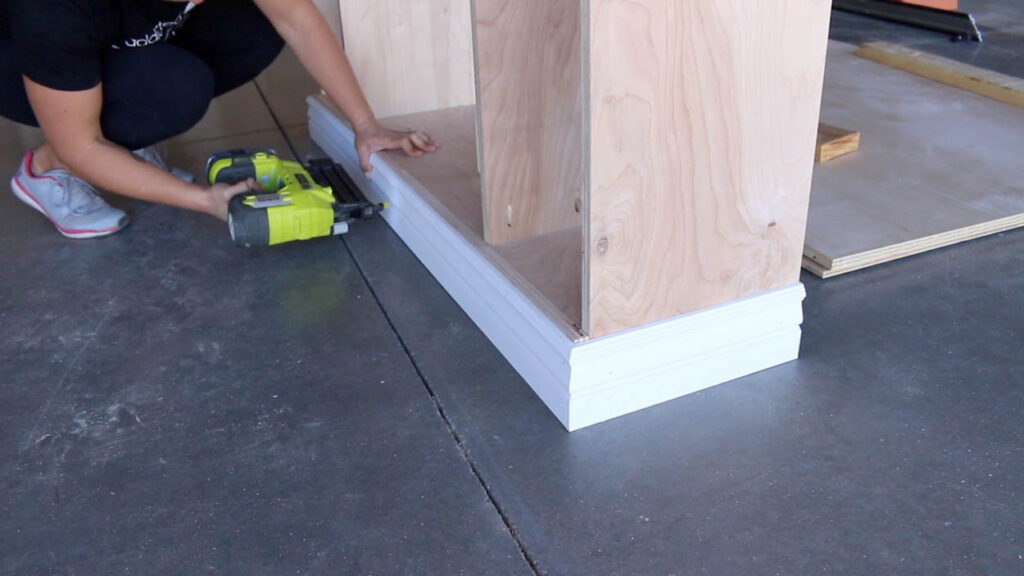 attaching base molding to the bottom of the DIY faux fireplace cabinet