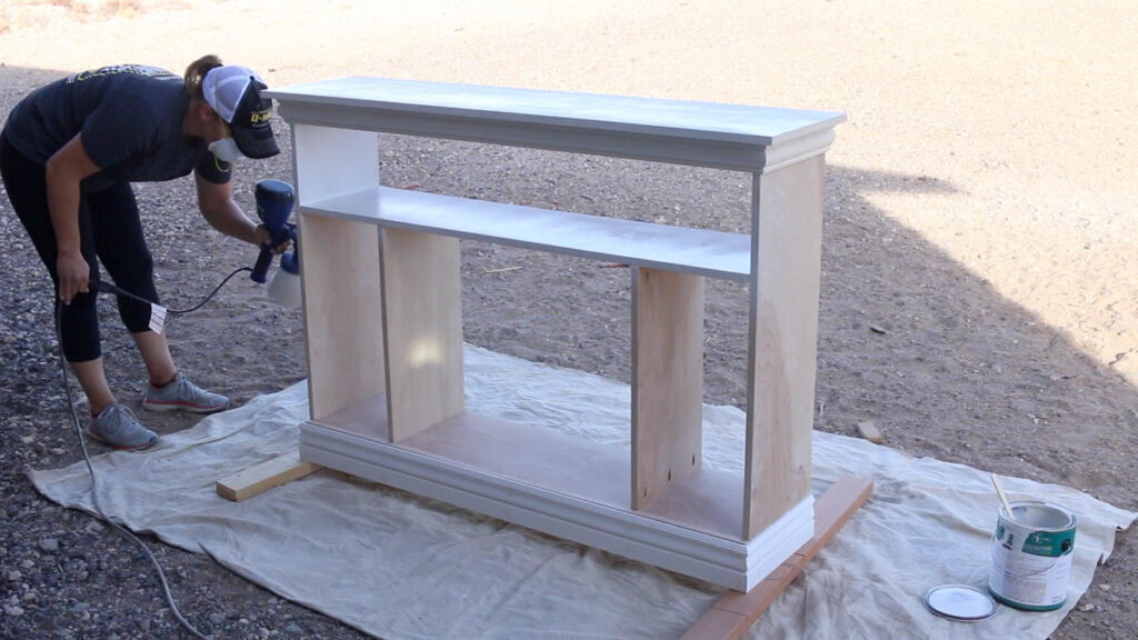 painting the DIY faux fireplace cabinet base using a paint sprayer outdoors