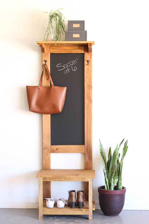 DIY rustic hall tree with chalkboard, coat hooks, bench, and shoe shelf against white wall