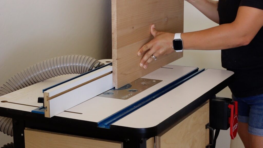 Running a side panel through a router table to cut a rabbeted groove for the cabinet back