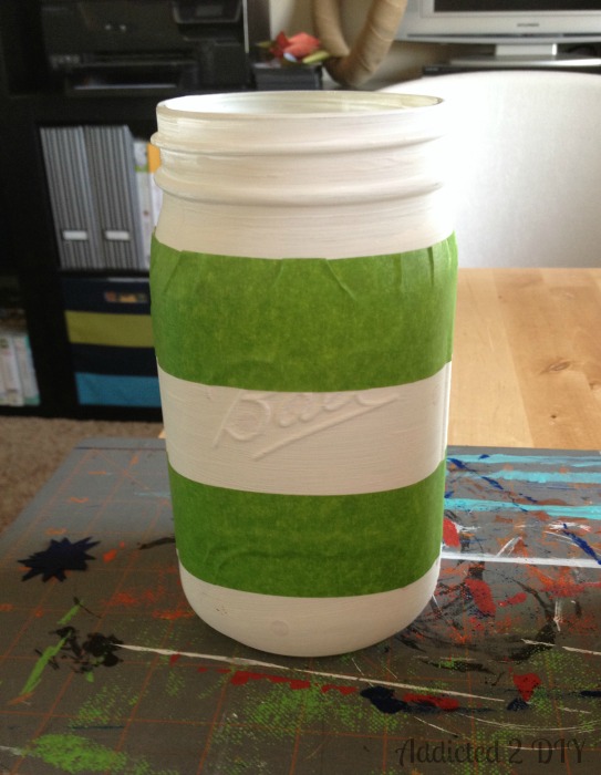 A quart-sized Ball mason jar with green Frog Tape applied in horizontal bands to mask off stripes before painting with red chalk finish paint.