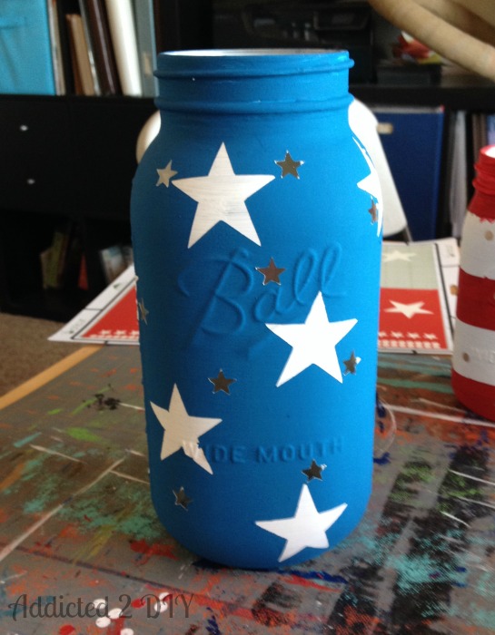 Half-gallon Ball mason jar painted in blue Americana Decor Chalky Finish paint with white and small star-shaped cutouts revealed after peeling vinyl resist.