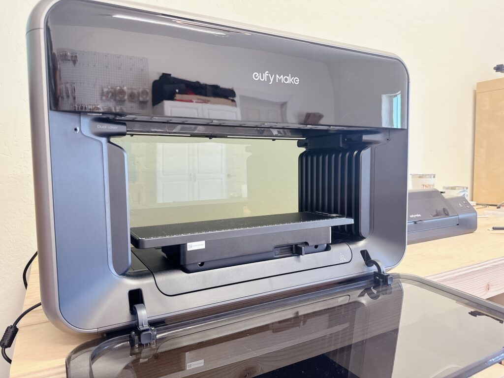 Interior view of the EufyMake E1 UV printer with the front cover open, showing the standard flatbed print surface and dual laser alignment system