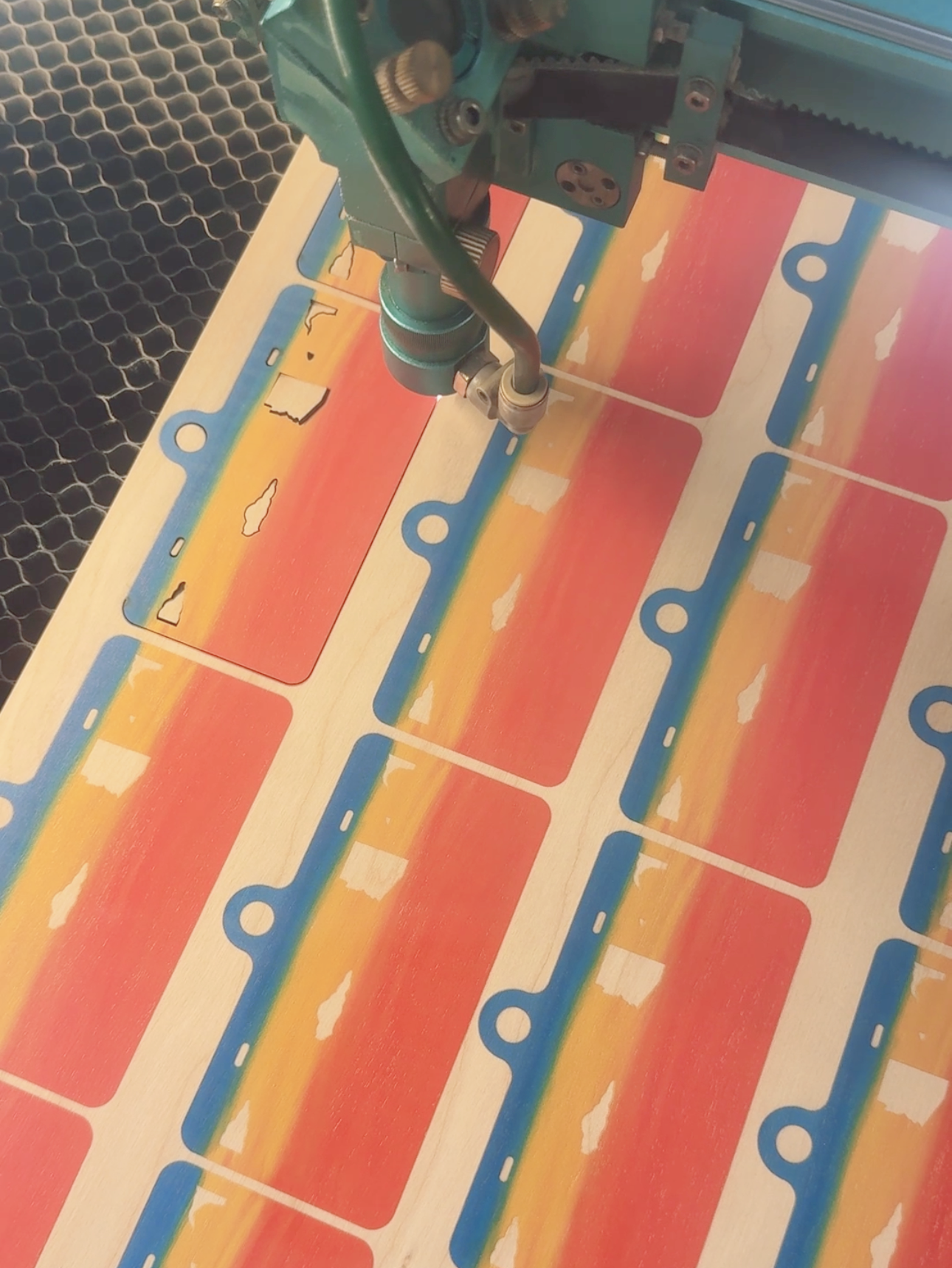 Sheet of wood with UV printed design being cut on a laser