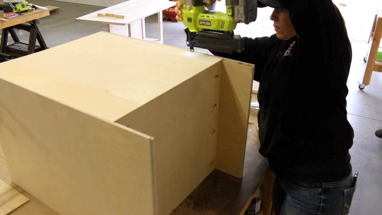 Nailing the plywood back panel onto a DIY cabinet carcass using a Ryobi brad nailer