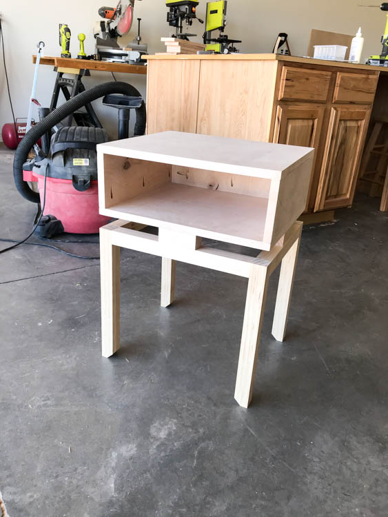 Unfinished plywood nightstand sitting on assembled wood base before painting