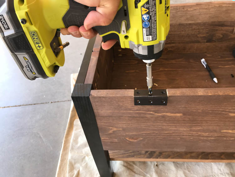 Attaching black hinges to the lid of a DIY storage bench using a drill