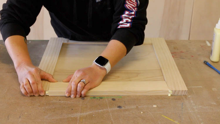 Assembling a tongue and groove cabinet door panel by hand on a workshop table