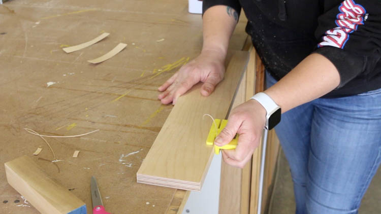 Trimming excess iron-on edge banding from a plywood drawer front using a plastic edge banding trimmer
