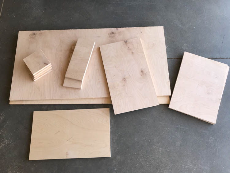 Cut plywood pieces for a DIY modern coffee table with storage drawer laid out on a garage floor before assembly.