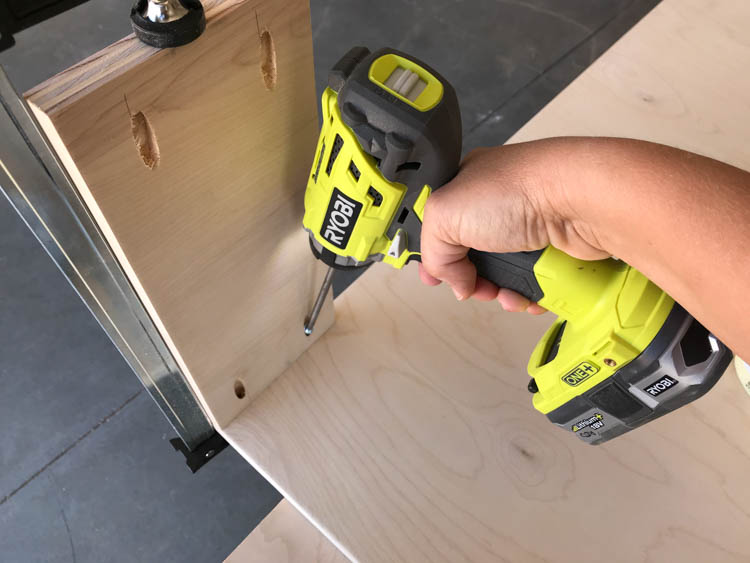 Hand using a Ryobi drill to drive pocket hole screws into the side panel of a plywood coffee table during assembly