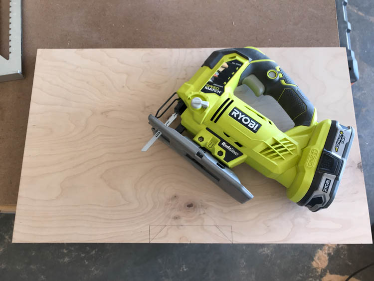 Ryobi jigsaw positioned on a plywood panel with pencil lines marking cutout for the drawer of the coffee table