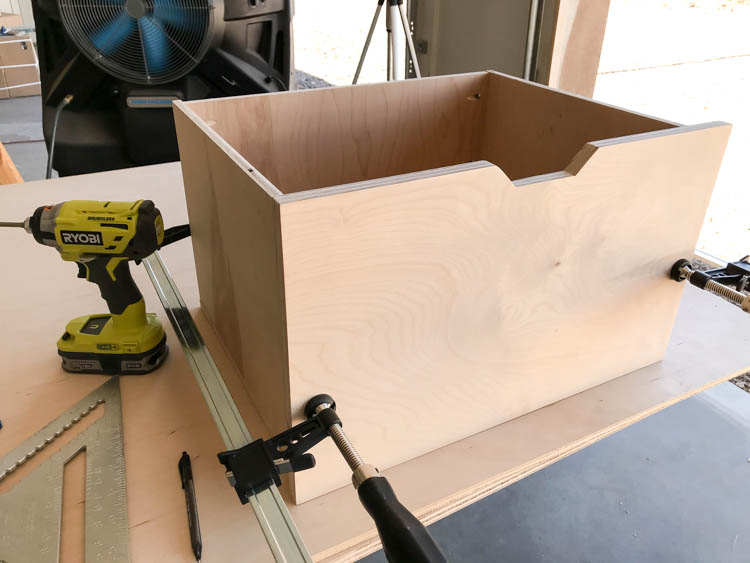 Assembled plywood coffee table drawer clamped to a workbench, showing the notched cutout in the front panel