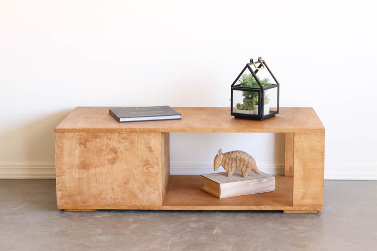 Finished DIY modern coffee table with a warm wood stain, open lower shelf, and hidden drawer, styled with a book and glass terrarium lantern