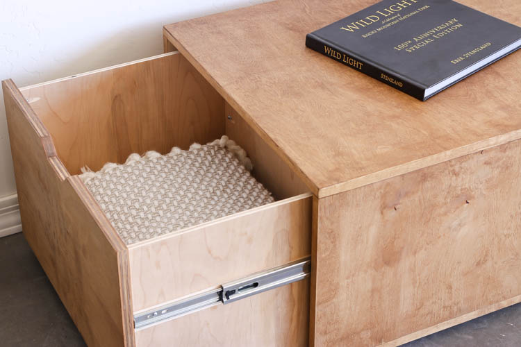 Close-up of the large hidden drawer pulled open on a DIY plywood coffee table, showing a folded blanket stored inside with ball-bearing drawer slides visible